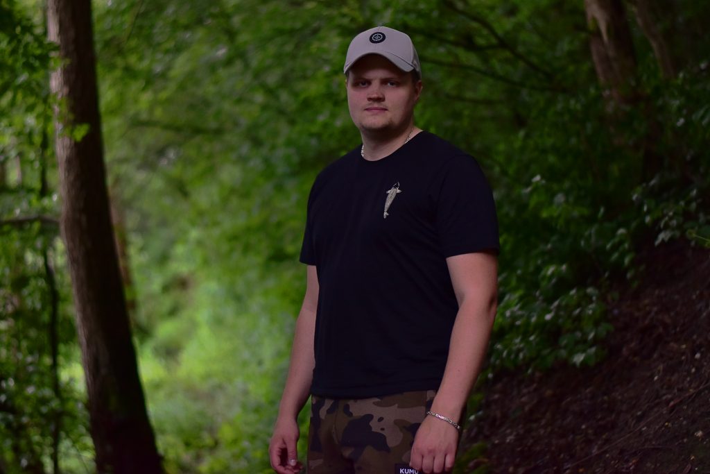 Domenic Kleinwächter, Gründer von PlatinCarpBase, im Wald in Freizeitkleidung mit Cap
