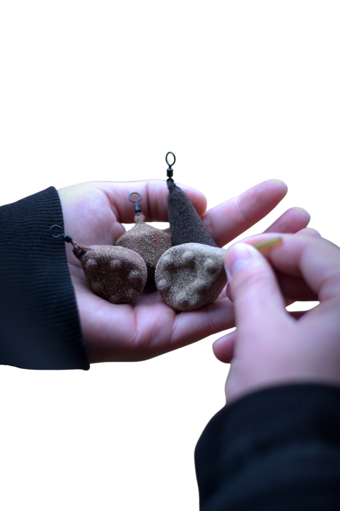 Hände halten mehrere Karpfenbleie im natürlichen Stein-Look für modernes Karpfenangeln.